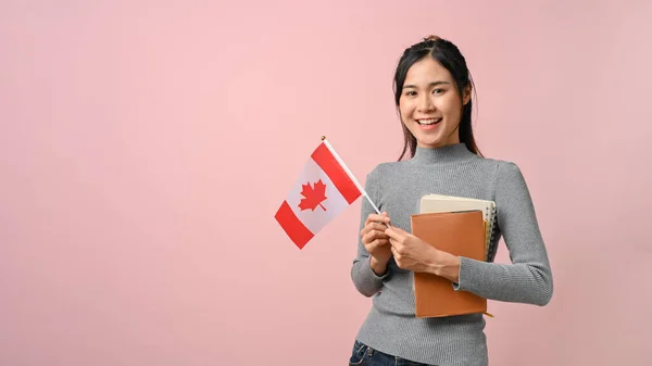 Confident Asian girl showing Canada flag on pink isolated background, education concept. study abroad concept.