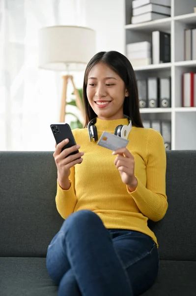 漂亮的亚洲女人一边拿着信用卡一边拿着手机上网购物 — 图库照片