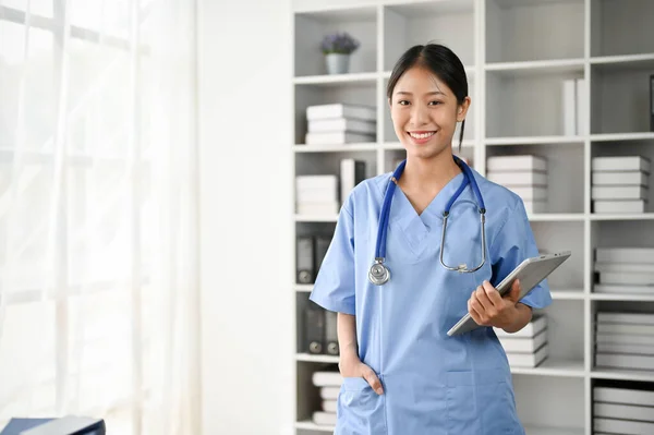 Portrait of young Asian medical student smiling and standing in the study room while holding tablet on her hand
