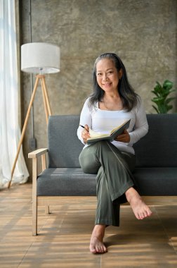 Yaşlı kadın evde kitap okuyor ve gülümsüyor, evde boş zamanlarının tadını çıkarıyor.. 