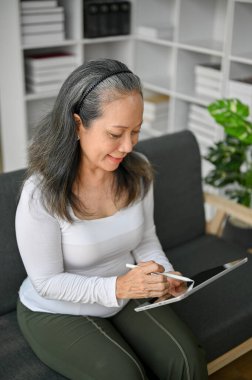 Evdeki kanepede otururken tablet kullanan yaşlı kadın. Boş zamanlarında dinleniyor..  