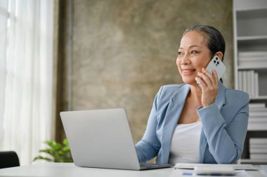 Kararlı ve profesyonel Asyalı iş kadını veya kadın CEO ofisinde masasında otururken iş müşterisiyle telefonda konuşuyor..