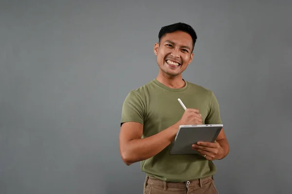 身穿休闲装 头戴数码平板电脑 面带微笑的千年亚洲人 站在灰蒙蒙的背景下 — 图库照片