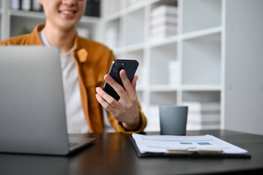 Akıllı genç iş adamının elinde akıllı telefon tutarken ofis odasında dizüstü bilgisayarla çalışmasını kapat.