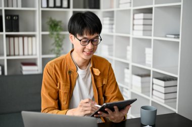 Çalışma odasındaki genç Asyalı üniversite öğrencilerinin bilgisayar dijital tablet ve ders kitaplarıyla görüntülerini kapat.. 