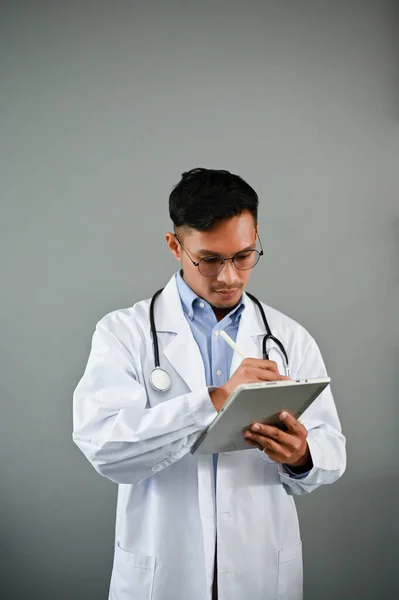 身穿听诊器制服的职业千年亚洲男性医生 站在孤立的灰色背景上 正在使用数码平板电脑 — 图库照片