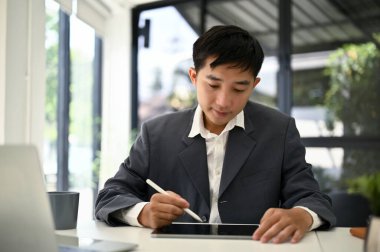 Yeni projesini masasında tablet üzerine planlayan Asyalı bin yıllık iş adamı..