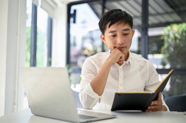 Düşünceli Asyalı iş adamı ofisteki masasında ajandasında bazı detaylar okuyor..