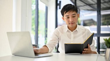 Yakışıklı ve zeki Asyalı iş adamı ajandasında toplantı programını kontrol ediyor ve masasında çalışıyor..