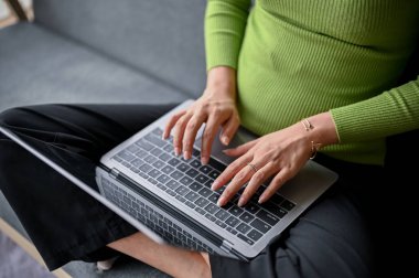 Asya 'lı genç bir kadının günlük kıyafetleriyle klavyeye yazı yazarken, oturma odasındaki kanepede dizüstü bilgisayarını kullanırken yakın plan görüntüsü. ev kavramından çalışma