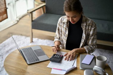 Güzel bir Asyalı kadın oturma odasındaki vergileri ve giderleri hesaplamaya odaklanıyor..