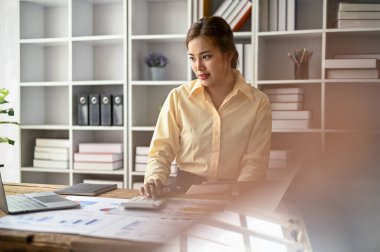 Profesyonel bir Asyalı iş kadını, yeni bir proje için bütçe hesaplayarak görevlerine odaklanıyor..