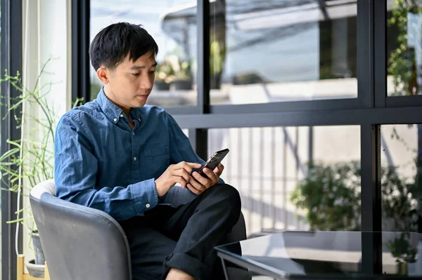 Pensativo Inteligente Hombre Asiático Milenario Usando Teléfono Inteligente Mientras Relaja — Foto de Stock