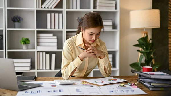 Stock image Professional and focused millennial Asian businesswoman or female boss reading and examining a new business model reports at her desk.