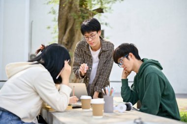 Zeki genç Asyalı üniversite öğrencisi arkadaşlarına kampüs parkında matematik ödevlerinde yardım etti..