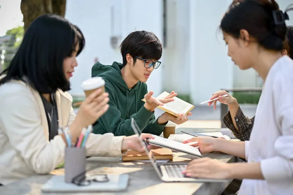 Image of a group of college students preparing for the exam together, A smart young Asian male college students helping and tutoring history to his friends at a campus park.