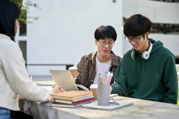 快乐而快乐的年轻亚洲男性大学生和他的朋友聊天时 和他的同伴坐在校园里的一张桌子旁 — 图库照片