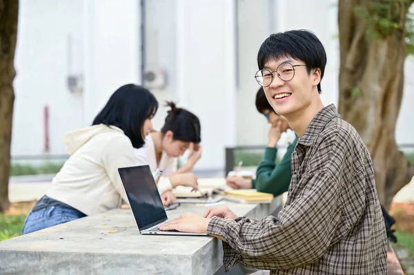 身穿休闲装 头戴笔记本电脑 面带微笑的年轻亚洲大学生和他的朋友们坐在校园公园的一张桌子旁 — 图库照片