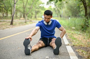 Yakışıklı Asyalı adam sokakta bacaklarını açıyor, doğa parkında koşmadan önce ısınıyor. Yaşam tarzı ve spor konsepti