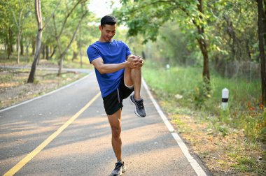 Yakışıklı ve formda spor giyimli Asyalı bir adam koşmadan önce bir sokakta bacağını esnetiyor. Isınmak ya da serinlemek. Koşu, maraton, koşu.