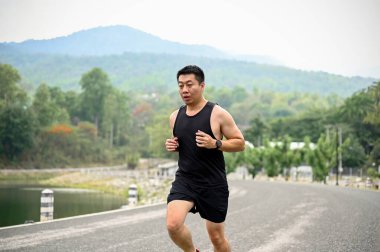 Hafta sonları halka açık bir parkta koşan yorgun ve yorgun Asyalı bir adam. Yaşam tarzı kavramı