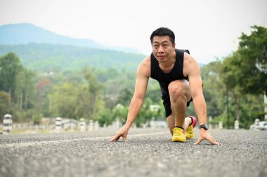 Sağlıklı formda, spor giyimli, olgun Asyalı adam başlangıç pozisyonunda, koşmaya hazırlanıyor..