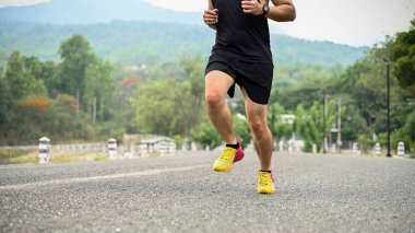 Kesilmiş görüntü, spor giyim ve profesyonel koşu ayakkabıları giyen Asyalı bir adam halka açık bir parkta yolda koşuyor..