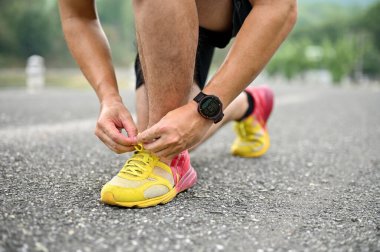 Spor ayakkabı bağcıklarını bağlayan, parkta koşmaya hazırlanan atletik bir adamın görüntüsü..