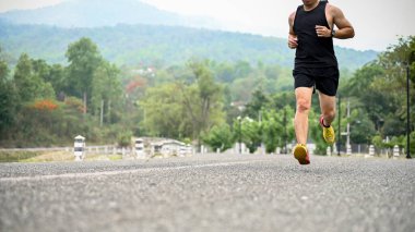 Kesilmiş görüntü, spor giyim ve profesyonel koşu ayakkabıları giymiş Asyalı bir adam halka açık bir parkta yolda koşuyor. Boş zaman ve spor konsepti
