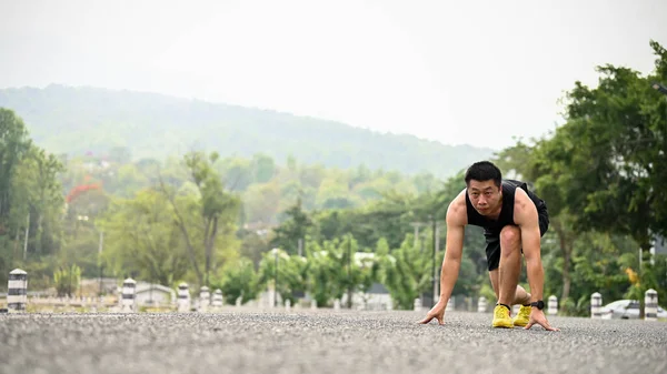 Spor giyim sektöründe kararlı ve odaklanmış olgun Asyalı adam başlangıç pozisyonunda koşmaya hazırlanıyor..