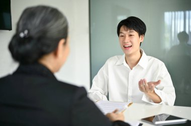 Kendine güvenen ve zeki Asyalı genç erkek aday bir iş görüşmesinde kariyer deneyimlerini bir iş bulucuya anlatıyor..