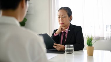 Profesyonel ve odaklanmış üst düzey Asyalı bayan İK yöneticisi ofiste bir iş adayıyla görüşüyor. İşe alım konsepti