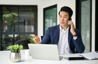 Profesyonel ve odaklanmış Asyalı iş adamları iş ortağıyla telefonda konuşuyor. Ofisinde çalışırken telefonda iş konuşuyorlar..