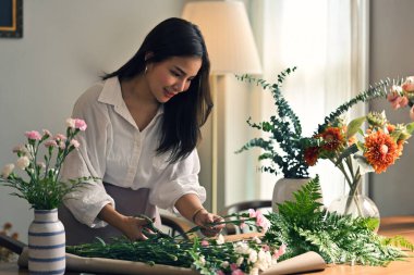Güzel ve çekici genç Asyalı kadın, evinde güzel çiçekli bir vazo düzenlemekten hoşlanıyor. Çiçekçilik atölyesine katılan güzel bir Asyalı kadın..
