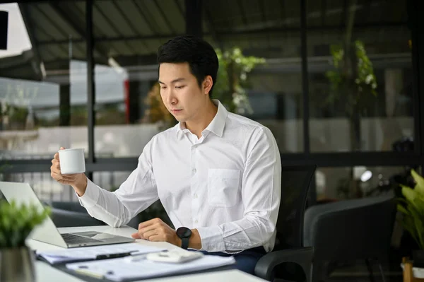 밀레니엄 아시아 사업가가 노트북으로 온라인 문서를 사무실에 책상에서 커피를 마시는 — 스톡 사진
