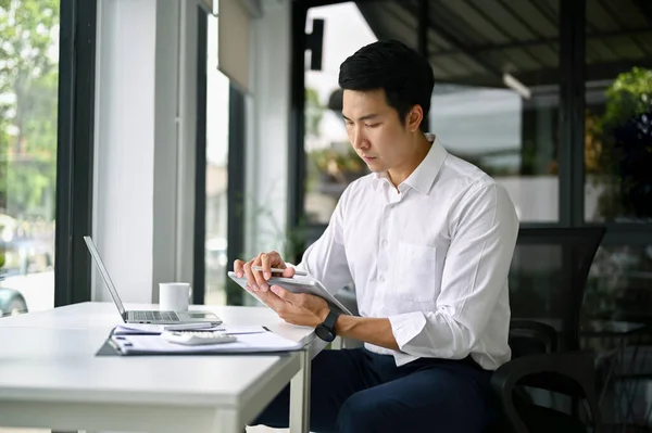 stock image Smart and focused millennial Asian businessman or male boss using his digital tablet at his desk in the office.