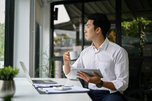 성공적 밀레니엄 아시아 사업가나 보스는 내다보면서 자신의 책상에서 커피를 들이마시면서 — 스톡 사진