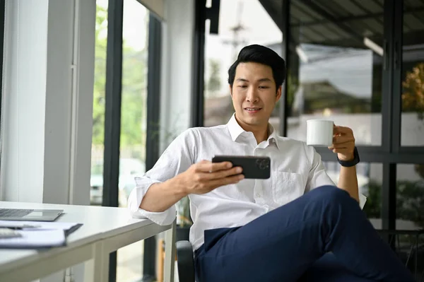Sonriente Relajado Empresario Asiático Milenario Viendo Videos Teléfono Inteligente Bebiendo — Foto de Stock