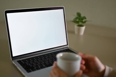 Evdeki dizüstü bilgisayarında çalışırken kahvesini yudumlayan bir kadının görüntüsü. grafik reklamlarınızı göstermek için dizüstü bilgisayar beyaz ekran modeli