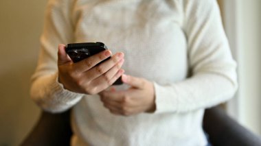 Beyaz kazaklı bir kadının kafeteryada serinlerken akıllı telefonunu kullanırken görüntüsü..