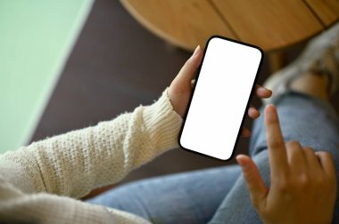Bir odada dinlenirken akıllı telefonunu kullanan, rahat beyaz kazaklı bir kadının yakın plan görüntüsü. akıllı telefon beyaz ekran modeli