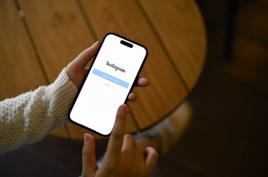 Chiang Mai, Tayland - 15 Mayıs 2023: Bir kafede dinlenirken Instagram hesabındaki bir kadının yakın plan resmi. iPhone ekranında Instagram logosu