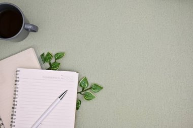 Yeşil arkaplanda metin veya ürününüzü göstermek için kalem, defter, kahve fincanı, bitki yaprağı ve kopya alanı ile en düşük çalışma alanı görünümü.