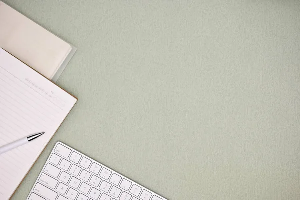 stock image Modern minimal office workspace with white keyboard, pen, notebook and empty space on green background. top view