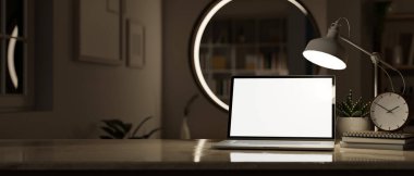 Laptop beyaz ekran maketi, masa lambası, çalar saat ve karanlık bir odanın bulanık arkaplanı ile gece ev çalışma alanının yakın görüntüsü. 3d görüntüleme, 3d illüstrasyon