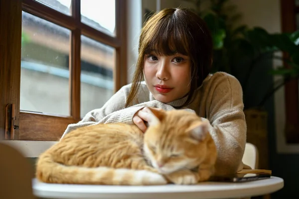 リビングのテーブルで可愛いオレンジ色の猫と一緒に休んでいる美しい若いアジアの女性の肖像画 ペットのコンセプト — ストック写真