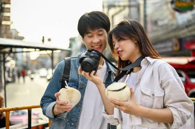 Mutlu genç Asyalı turist çiftimiz şehri gezerken fotoğraflarına bakıyorlar. Seyahat, tatil, Asya gezisi.