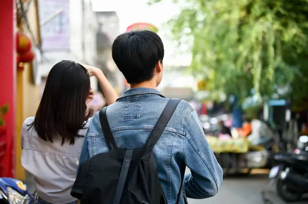 stock image Happy young Asian tourist couple enjoys taking photos and sightseeing the Chiang Mai old town market together. back view image. Lifestyle concept