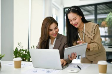 Meslektaşına tablet ekranda bir şey gösteren Asyalı profesyonel bir ofis çalışanı ofiste yeni bir projeyi tartışıyor ve planlıyor. Takım çalışması, ortak çalışma konsepti
