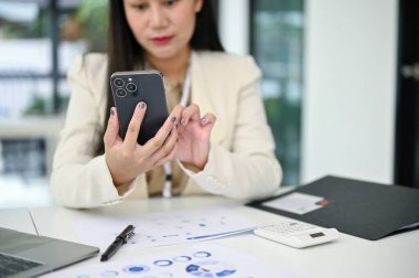 Asyalı profesyonel bir iş kadını ya da kadın muhasebecinin masasındaki akıllı telefonu kullanarak yakın plan görüntüsü..